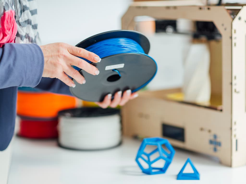 Person loading a spool of blue filament into a wooden frame 3D printer
