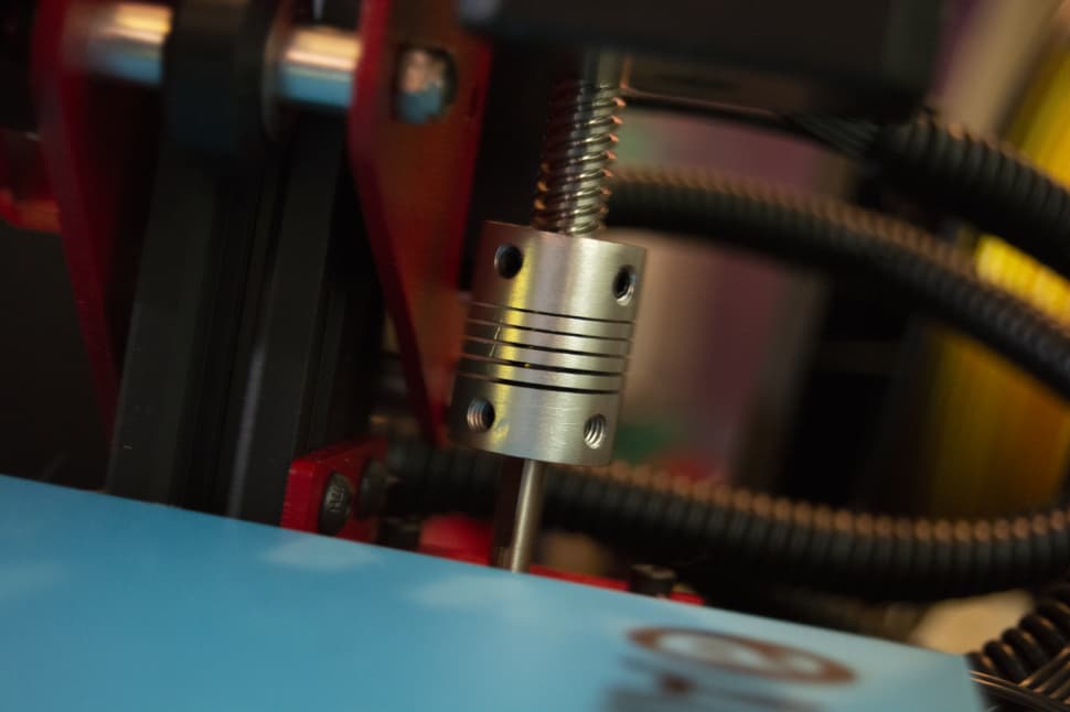Close up of a 3D printer hot end moving above a blue print bed