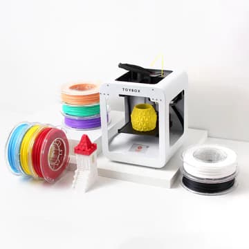 Toybox 3D printer beside a stack of colored filament spools
