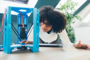 A woman operating a blue delta style 3D printer in a home studio