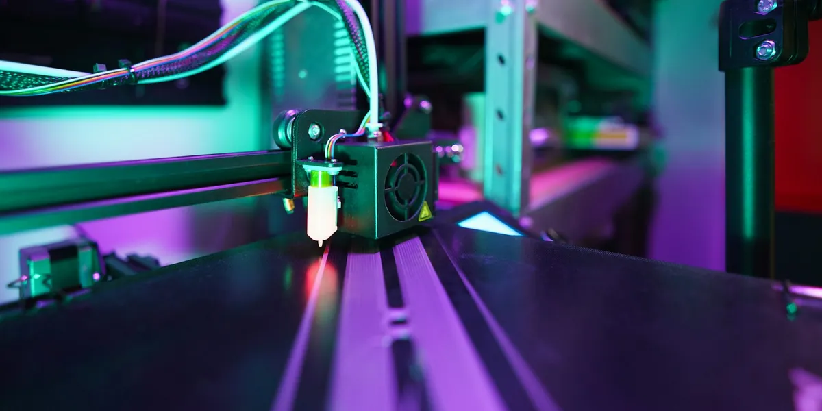 3D printer nozzle moving over a black print bed under purple and green workshop lights